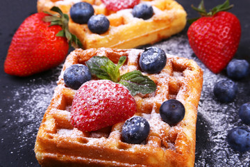 Homemade Traditional belgian waffles with fresh fruit, berries and sugar powder on black plate.
