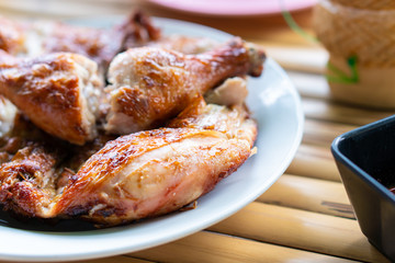 Chicken marinated with spices then grilled until cooked. Chopped into pieces, placed on a plate on a bamboo table with a medium spicy sauce.