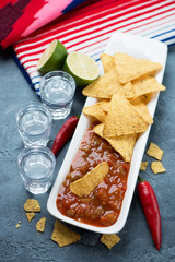 Nachos, salsa sauce and tequila shots over blue stone surface with mexican poncho in the background