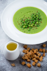 Green peas cream-soup served in a white plate, vertical shot over light-grey stone surface