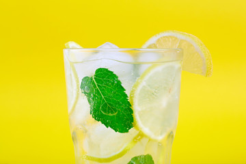Mojito cocktail with lemon and mint in highball glass, on a yellow background.