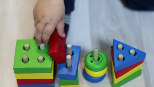 One year old child (boy) plays with geometric sorter (wooden constructor), close-up of child's hand and toy, 50 fps, slow motion