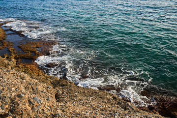 Aerial top view of sea waves hitting rocks on the beach with turquoise sea water. Amazing rock cliff seascape in the coastline. Aerial view of sea waves and fantastic Rocky coast. Mediterranean Sea.