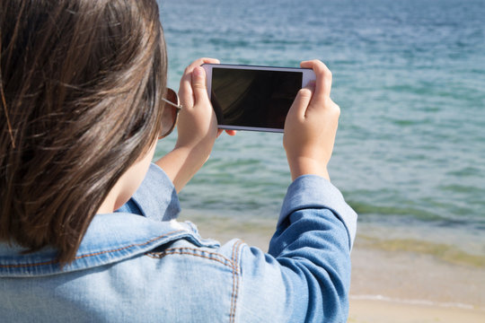 Girl Taking Picture With The Mobile Phone Of The Beach And The Sea