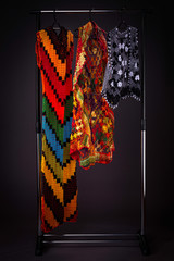 Full size stand alone hanger with colourful handmade embroidery wardrobe with a rainbow dress and vests on a hanger against a clean grey background