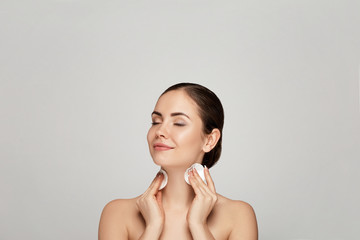 Obraz premium Beauty portrait of a cheerful young topless woman removing face make-up with a cotton pad
