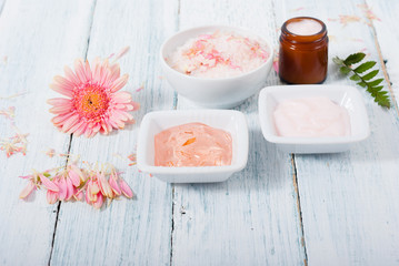 Fototapeta na wymiar beauty product samples, cosmetic cream, bath salt, liquid soap and pink flower, white wood table
