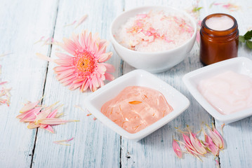 beauty product samples, cosmetic cream, bath salt, liquid soap and pink flower, white wood table