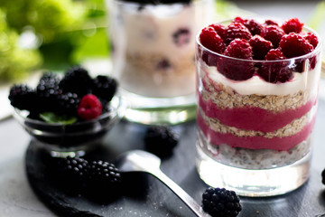 Healthy nutrition Dietary desserts. Glasses are filled with cottage cheese cream, in them chia seeds, raspberries, blueberries, blackberries. Near for background flowers.