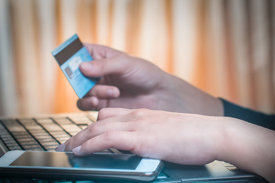 Image of the hands of a girl holding a smartphone and a credit card shopping online on a laptop.