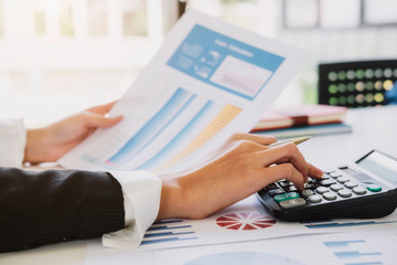 asian businesswoman or accountant working pointing graph discussion and analysis data charts and graphs and using a calculator to calculate  numbers.Business finances and accounting concept