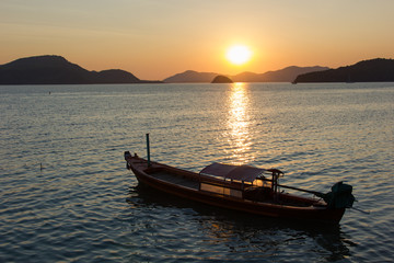 Fototapeta na wymiar Colorful Sunset on Phuket Island in Thailand. This photograph was taken at a beach in Panwa. It shows the mountains and a traditional boat in the image.