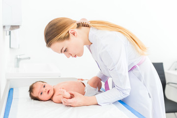 Obraz na płótnie Canvas Beautiful young female blonde pediatrician doctor examines baby girl checking her skin