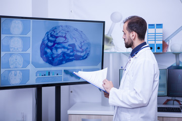 Doctor with clipboard on his hand looking at a brain on a big monitor
