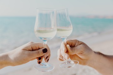Two hands holding glasses with white wine on sea background in Italy.