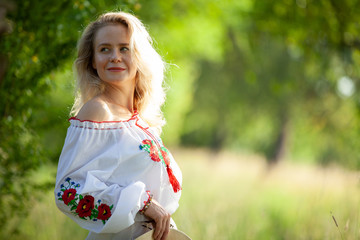 Fototapeta na wymiar Blonde girl in national Ukrainian dress posing on a background of village landscapes