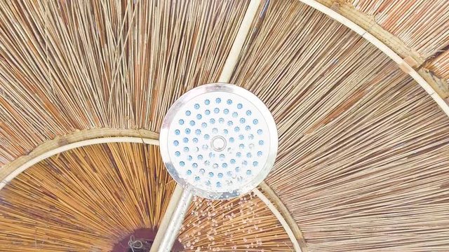 Doccia sotto all'ombrellone di paglia con acqua che cade sulla telecamera.