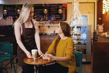 Young pretty woman and waitress in cafe.