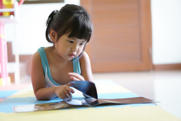 asian child cute or kid girl lie down with learning for reading a story book or tale and cartoon on the floor with enjoy and happy at library home or nursery and preschool for education