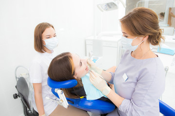 a woman dentist with an assistant treats a tooth to a woman in a modern dental clinic