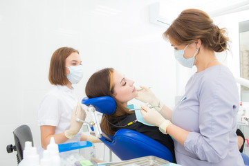 Fototapeta premium a woman dentist with an assistant treats a tooth to a woman in a modern dental clinic