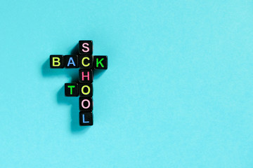 Back to school text from colorful letters on black cubes laid out in form of crossword puzzle, blue background. Concept education and beginning of schoolyear Copy space Top view Flat lay Layout