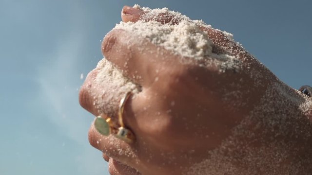 Close up of woman hands with ethnic jewellery dissolve white sand trough palm