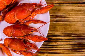 Plate with boiled crayfishes on wooden table. Top view