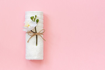 White towel roll tied with rope with sprig of orchid flower on pink paper background. Copy space Template for lettering text or your design