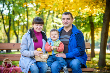Fototapeta premium happy family enjoying autumn picnic. Father mother and son sit on bench with apples basket. Happy family leisure together concept