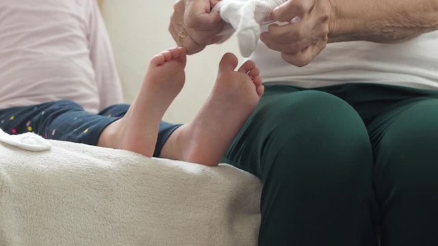 Elderly hands putting socks on girl's leg.