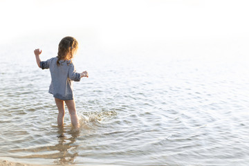 Fototapeta na wymiar Happy child running and jumping in the waves during summer vacation. Holiday on sea or ocean coast for family with young children.