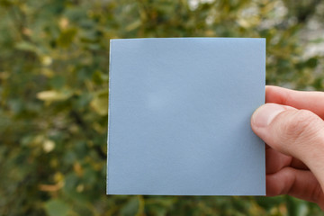 male fingers hold a blank blue sticker. square paper with space for text in the hand of a young man, close-up. selective focus. sticky note in a hand.