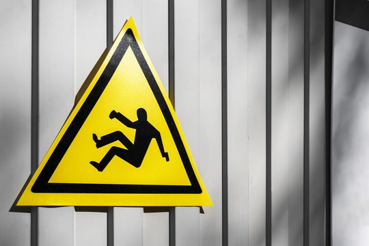 Yellow traffic sign warning for danger of falling on the gray iron fence, close-up. Fall danger or Slippery floor sign. falling man - sign of danger of falling because of construction