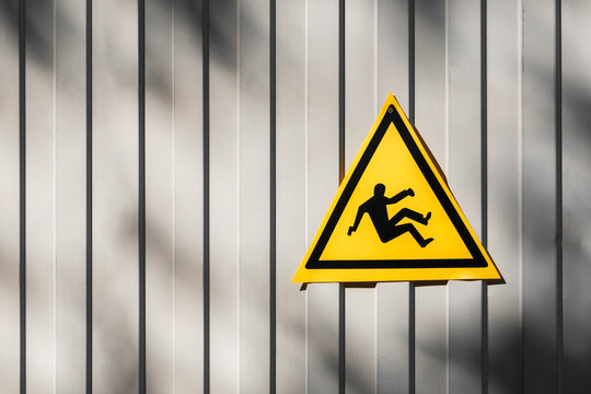 Yellow triangular road sign warning for risk of falling hanging on the gray fence. triangular traffic sign warning for danger of falling or steep grade. Yellow falling man -Warning hazard sign.
