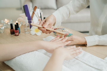Obraz na płótnie Canvas Manicure process at home service. focus on hands of two young asian women worker and customer in living room. Doing manicure nail file by wooden brush to clean up finger on table with candles beside.