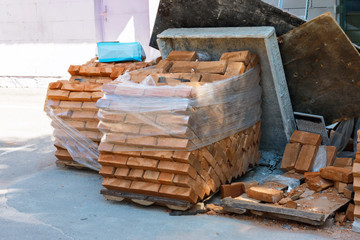 packs of orange bricks in the plastic protective film are near the construction site. orange Clay bricks in plastic film are stacked into cubes and stand in the backyard