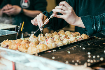 close up view of chef hands in process cooking takoyaki on hot pan. Famous food Osaka Japan street vendor. tasty japanese snack octopus balls selling in tsutenkaku.