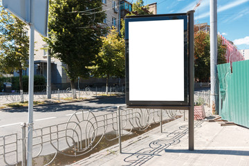 citylight with blank screen stands on the empty street near a construction site. empty white vertical billboard near the fence and pedestrian road. blank street poster or a lightbox with mock up space