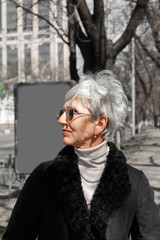 street close-up fashion style portrait of stylish caucasian middle-aged woman with gray hair wearing sunglasses, vertical image.