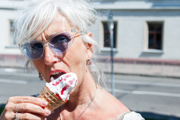 gray-haired middle-aged woman with glasses eats cherry ice cream in a waffle ice cream cone on the...