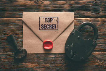 Top secret documents in envelope, rusty padlock and a key on a wooden table flat lay background....
