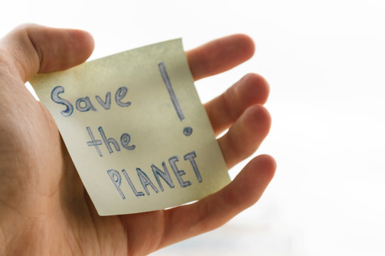 an appeal to save the planet earth is written on a piece of paper, blurred image. handwritten inscription save the planet on a square piece of paper in the male hand