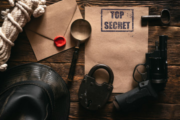 Top secret information mockup, leather hat, weapon, magnifying glass and rope on a wooden table of...