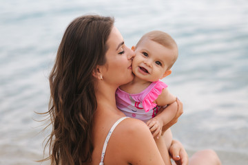 Mom kiss her little daughter on the beach. Backgound of sea