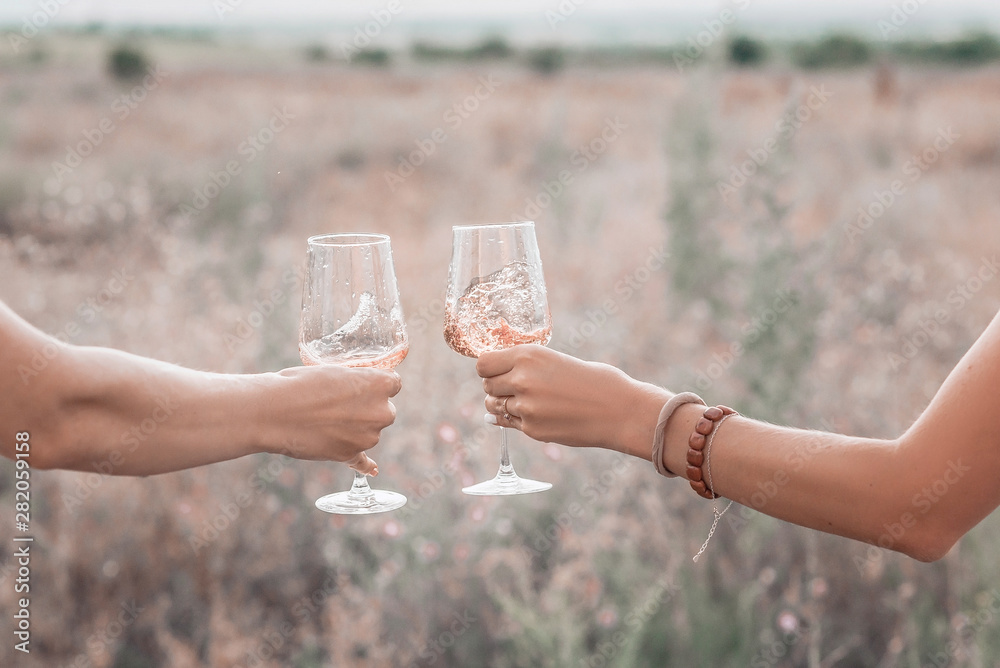 Wall mural two glasses of pink wine in women's hands on the sunset picnic.