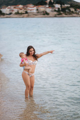 Mother hold baby on hands on the beach in the sea. Mom and daughter in swimsuit