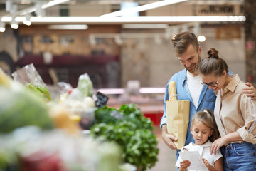 Waist up portrait of contemporary young family shopping for groceries at farmers market, copy space
