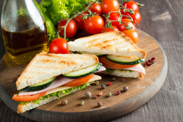 Close-up photo of a club sandwich. Sandwich with meat, prosciutto, salami, salad, vegetables, lettuce, tomato, onion and mustard on a fresh sliced rye bread on wooden background. Olives background.