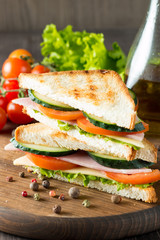 Close-up photo of a club sandwich. Sandwich with meat, prosciutto, salami, salad, vegetables, lettuce, tomato, onion and mustard on a fresh sliced rye bread on wooden background. Olives background.